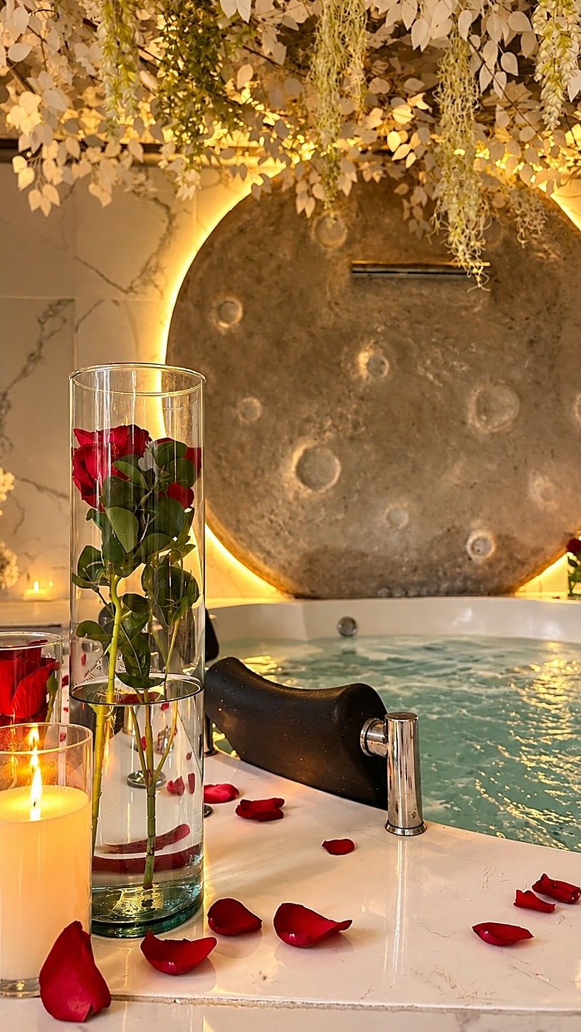 Jacuzzi de Garden SPA con pétalos de rosa y velas, frente a un disco dorado iluminado y bajo flores blancas colgantes