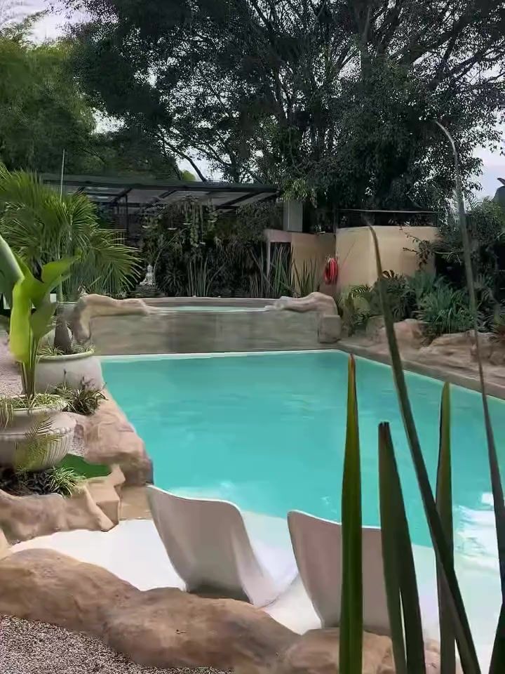 La piscina de Garden SPA: agua turquesa entre rocas, asoleadoras blancas dentro del agua y árboles alrededor